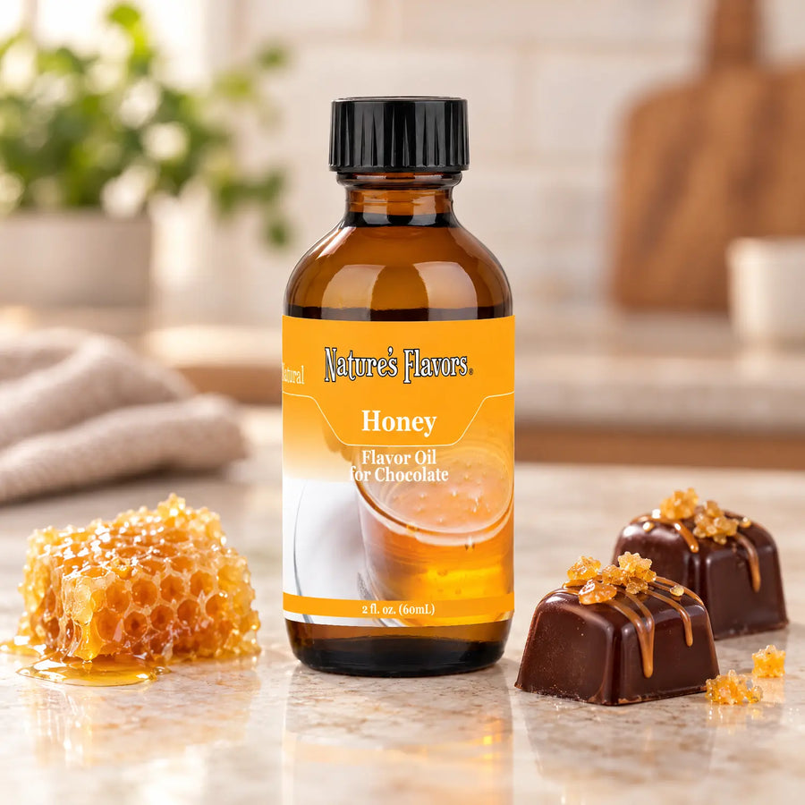 Nature's Flavors Honey Flavor Oil for Chocolate bottle beside golden honeycomb and dark chocolate bonbons on a light countertop.