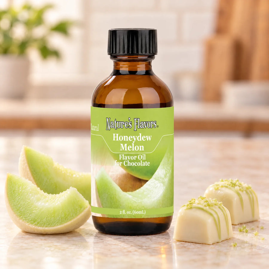 Nature's Flavors Honeydew Melon Flavor Oil for Chocolate bottle beside honeydew melon wedges and white chocolate bonbons on a light countertop.