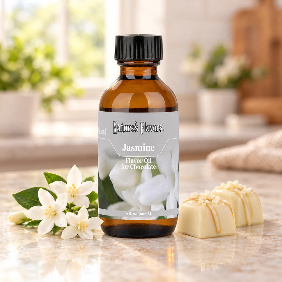 Nature's Flavors Jasmine Flavor Oil for Chocolate bottle beside white jasmine blossoms and white chocolate bonbons on a light countertop.