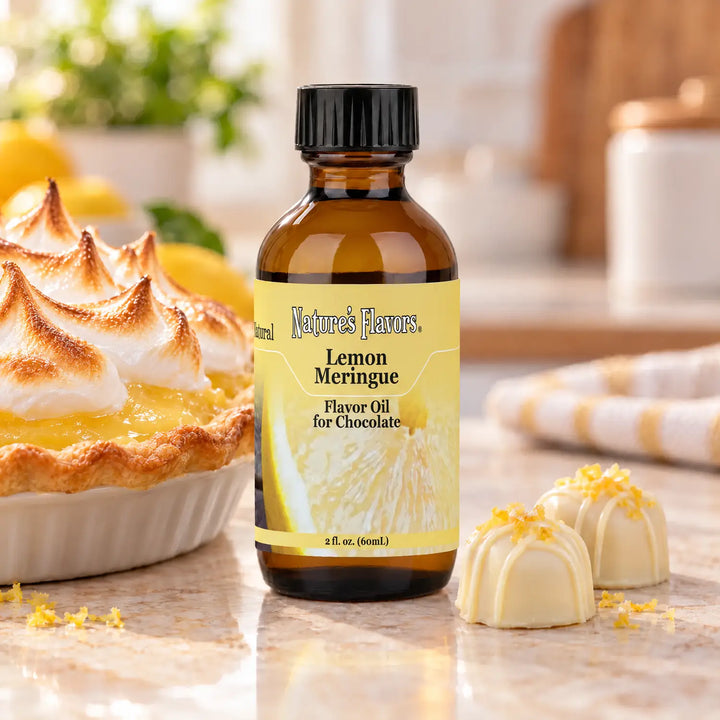 Nature's Flavors Lemon Meringue Flavor Oil for Chocolate bottle beside a large lemon meringue pie in a white dish and two white chocolate bonbons.