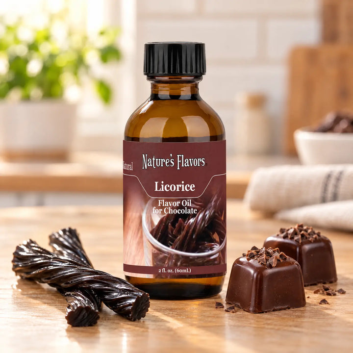 Nature's Flavors Licorice Flavor Oil for Chocolate bottle beside black licorice twists and dark chocolate bonbons on a wooden countertop.