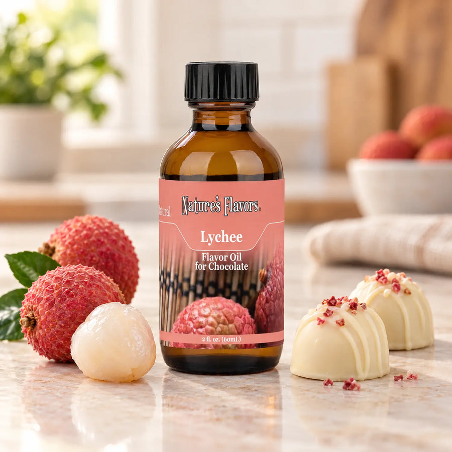 Nature's Flavors Lychee Flavor Oil for Chocolate bottle beside whole and peeled lychees and white chocolate bonbons.