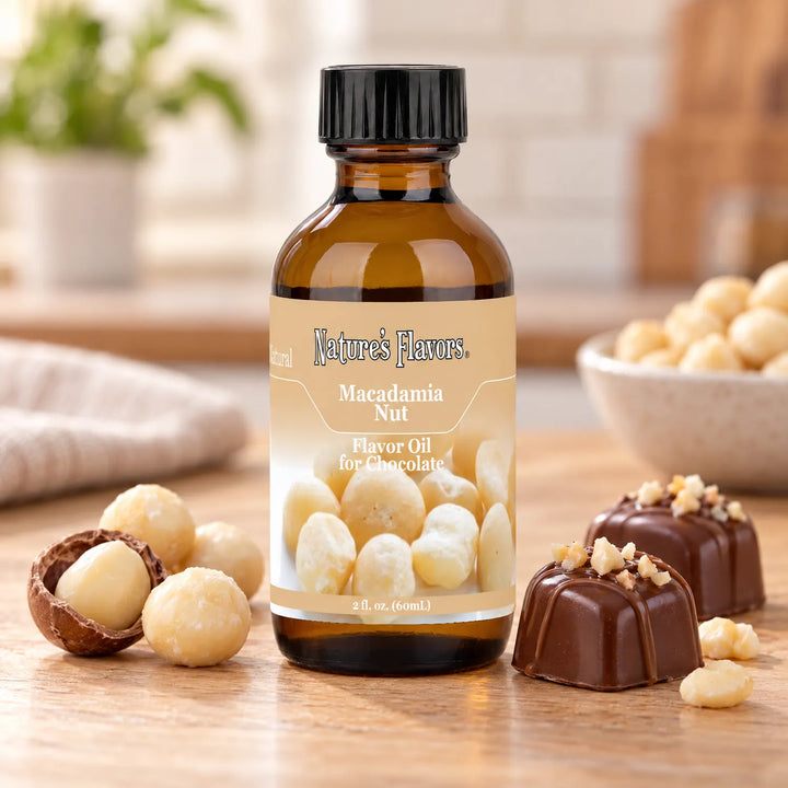 Nature's Flavors Macadamia Nut Flavor Oil for Chocolate bottle beside macadamia nuts, an open shell, and chocolate bonbons on a wooden countertop.
