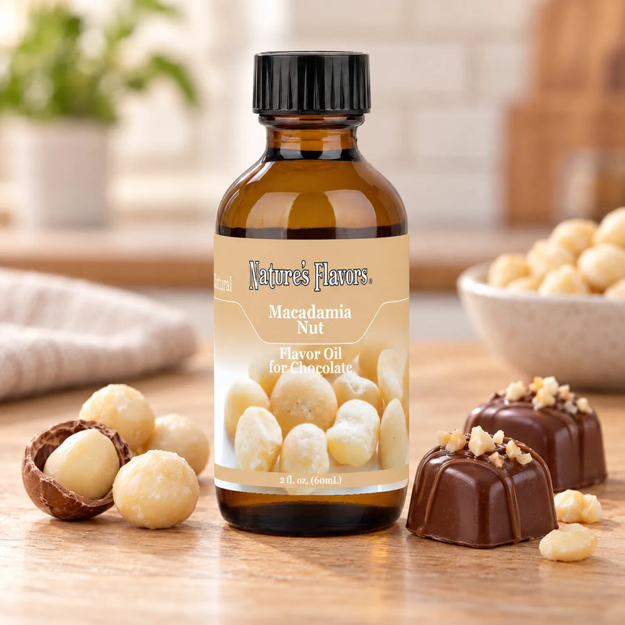 Nature's Flavors Macadamia Nut Flavor Oil for Chocolate bottle beside macadamia nuts, an open shell, and chocolate bonbons on a wooden countertop.