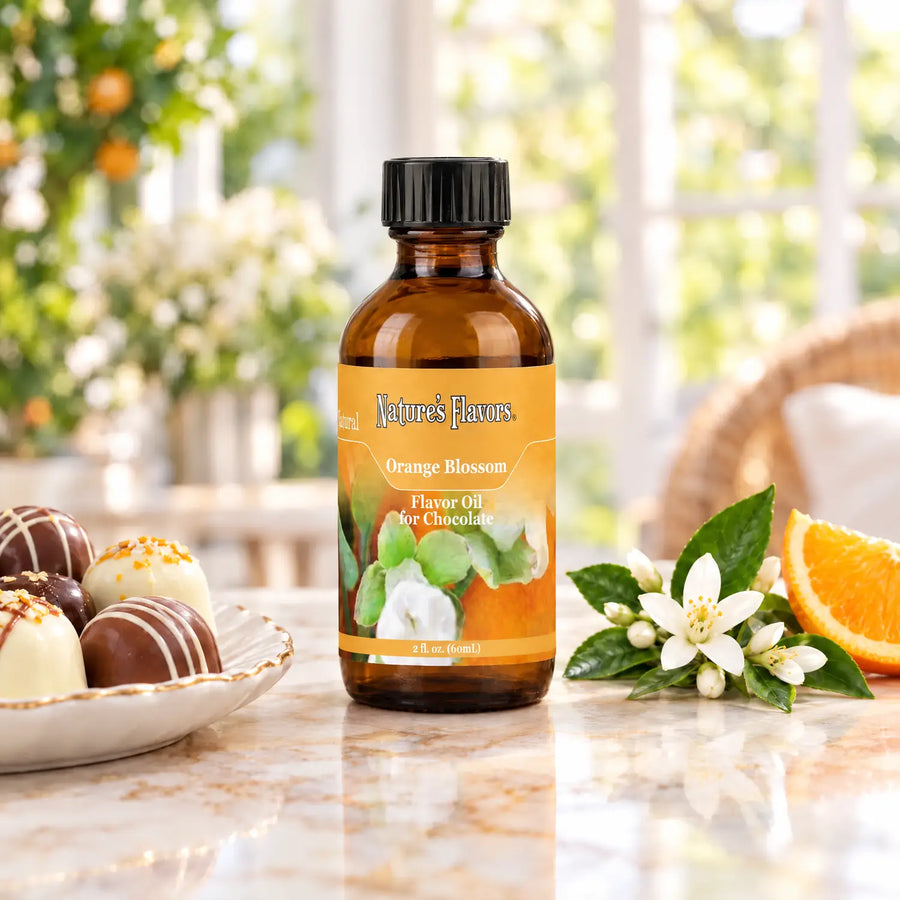 Nature's Flavors Orange Blossom Flavor Oil for Chocolate, 2-ounce bottle, with orange blossoms and chocolate bonbons on marble.
