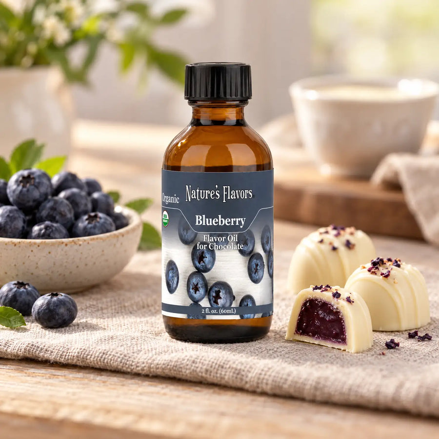 Nature's Flavors Organic Blueberry Flavor Oil for Chocolate bottle beside blueberries and white chocolate bonbons on a linen tasting table.
