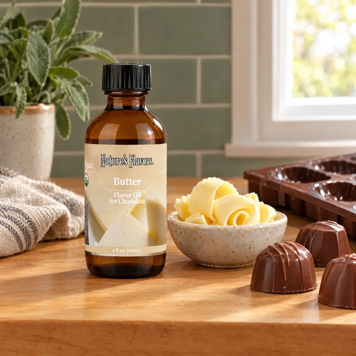 Nature's Flavors Organic Butter Flavor Oil For Chocolate, 2-ounce bottle, with butter curls and milk chocolate bonbons in a kitchen.