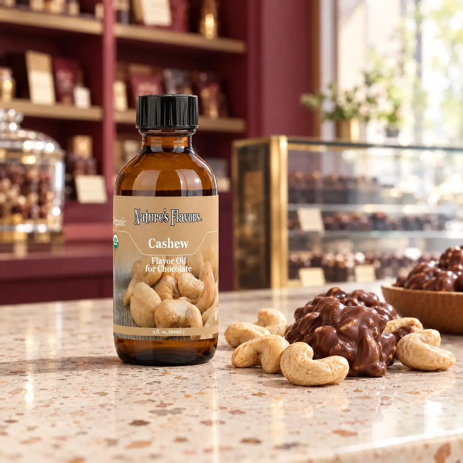 Nature's Flavors Organic Cashew Flavor Oil For Chocolate, 2-ounce bottle, with cashews and chocolate cashew clusters in a chocolate shop.