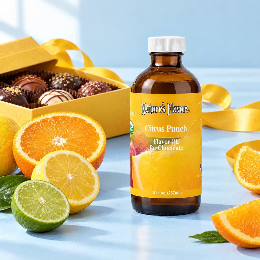Nature's Flavors Organic Citrus Punch Flavor Oil For Chocolate, 8-ounce bottle, with citrus slices and boxed chocolates on a gift table.