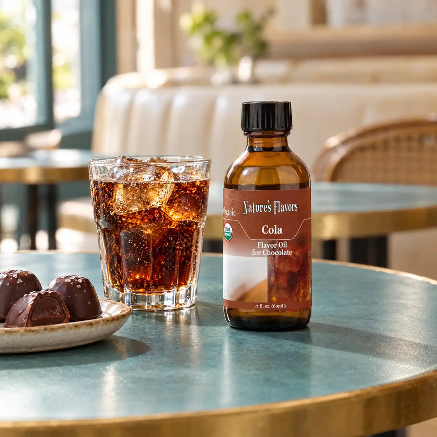 Nature's Flavors Organic Cola Flavor Oil For Chocolate, 2-ounce bottle, with cola and dark chocolate bonbons on a cafe table.