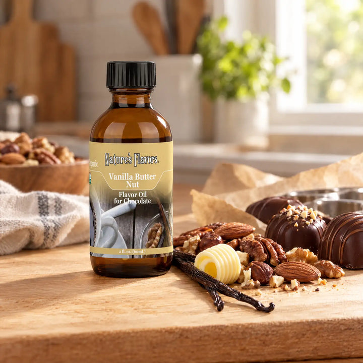 Nature's Flavors Organic Compliant Vanilla Butter Nut Flavor Oil For Chocolate, 2-ounce bottle, with vanilla, butter, nuts and chocolate bonbons in a kitchen.