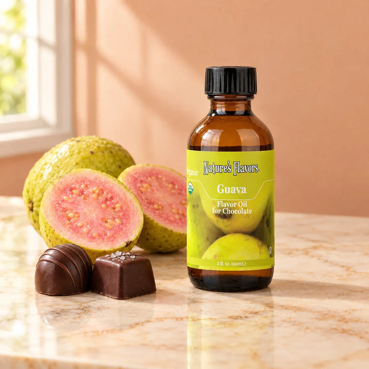 Nature's Flavors Organic Guava Flavor Oil For Chocolate, 2-ounce bottle, with pink guava halves and chocolate bonbons on marble.