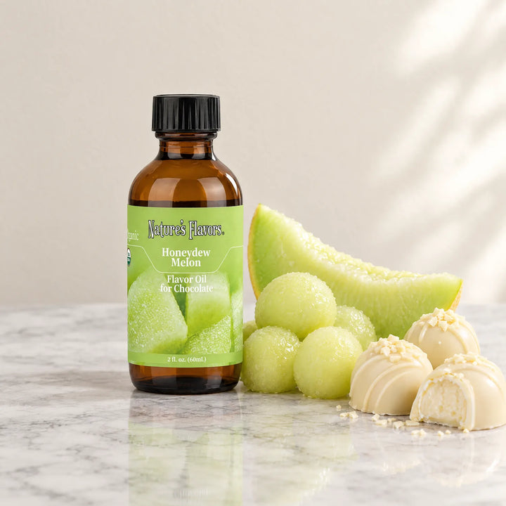 Nature's Flavors Organic Honeydew Melon Flavor Oil For Chocolate, 2-ounce bottle, with honeydew melon and white chocolate bonbons on marble.