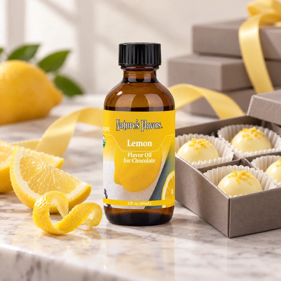 Nature's Flavors Organic Lemon Flavor Oil for Chocolate bottle beside lemon, curled peel, and a gift box of white chocolate truffles.