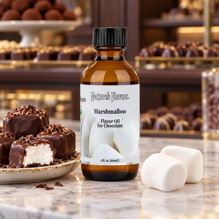Nature's Flavors Organic Marshmallow Flavor Oil for Chocolate bottle beside marshmallows and chocolate-covered squares in a chocolate shop.