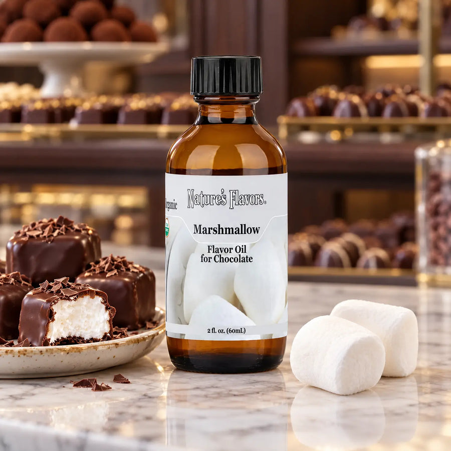 Nature's Flavors Organic Marshmallow Flavor Oil for Chocolate bottle beside marshmallows and chocolate-covered squares in a chocolate shop.