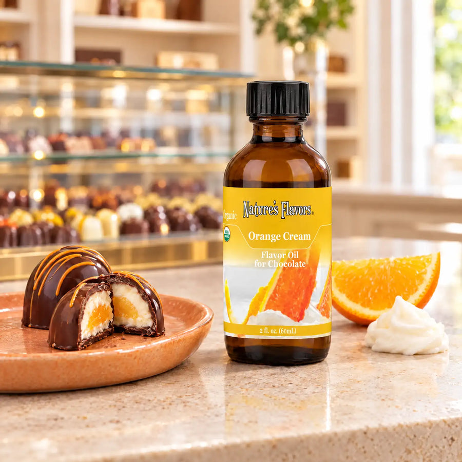 Nature's Flavors Organic Orange Cream Flavor Oil For Chocolate, 2-ounce bottle, with orange and cream-filled chocolates in a chocolate shop.