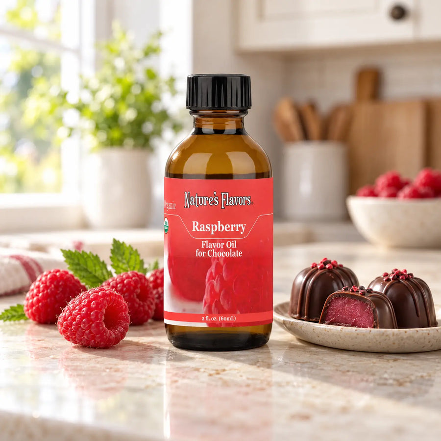 Nature's Flavors Organic Raspberry Flavor Oil for Chocolate bottle beside fresh raspberries and chocolate truffles on a kitchen counter.