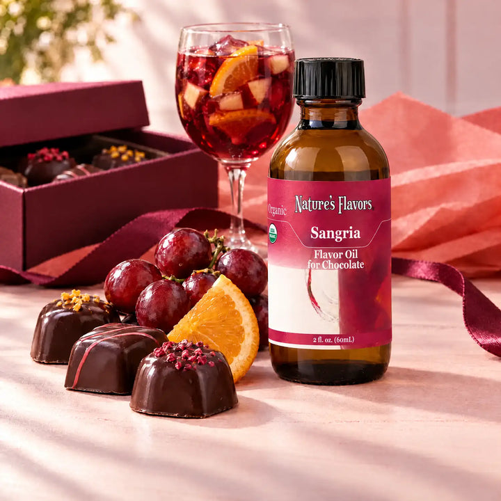 Nature's Flavors Organic Sangria Flavor Oil For Chocolate, 2-ounce bottle, with a glass of red sangria, grapes, orange and boxed chocolates on a gift table.