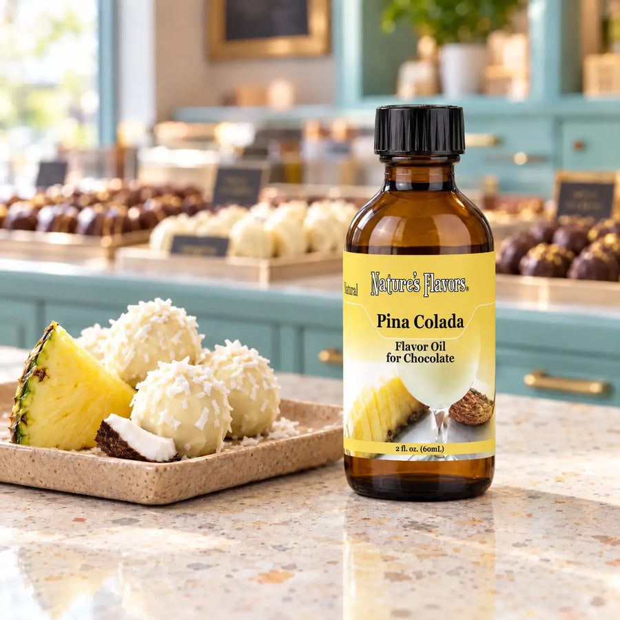 Nature's Flavors Pina Colada Flavor Oil for Chocolate, 2-ounce bottle, with pineapple, coconut and white chocolate truffles in a chocolate shop.