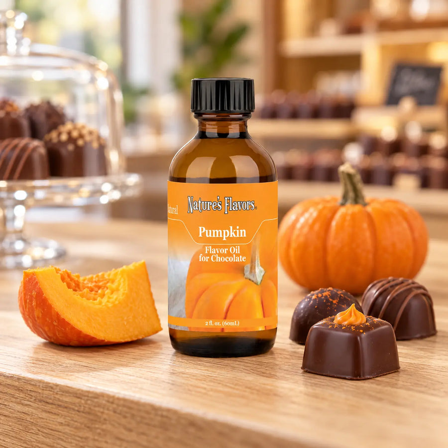 Nature's Flavors Pumpkin Flavor Oil for Chocolate bottle beside a pumpkin wedge, a small pumpkin, and chocolates on a boutique counter.