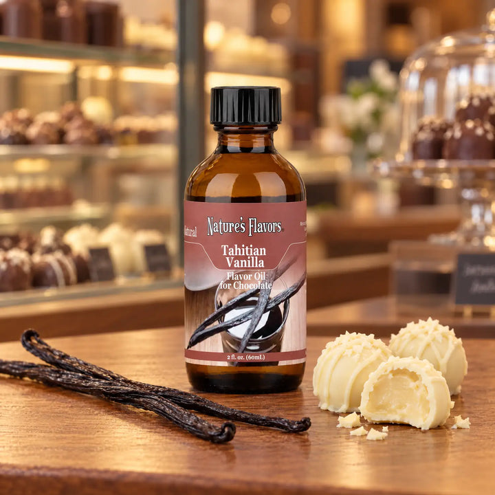 Nature's Flavors Tahitian Vanilla Flavor Oil for Chocolate bottle beside vanilla beans and white chocolate truffles on a boutique counter.