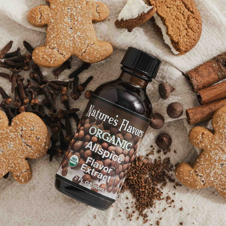 Nature's Flavors Organic Allspice Flavor Extract bottle surrounded by gingerbread cookies and spices on a textured surface.