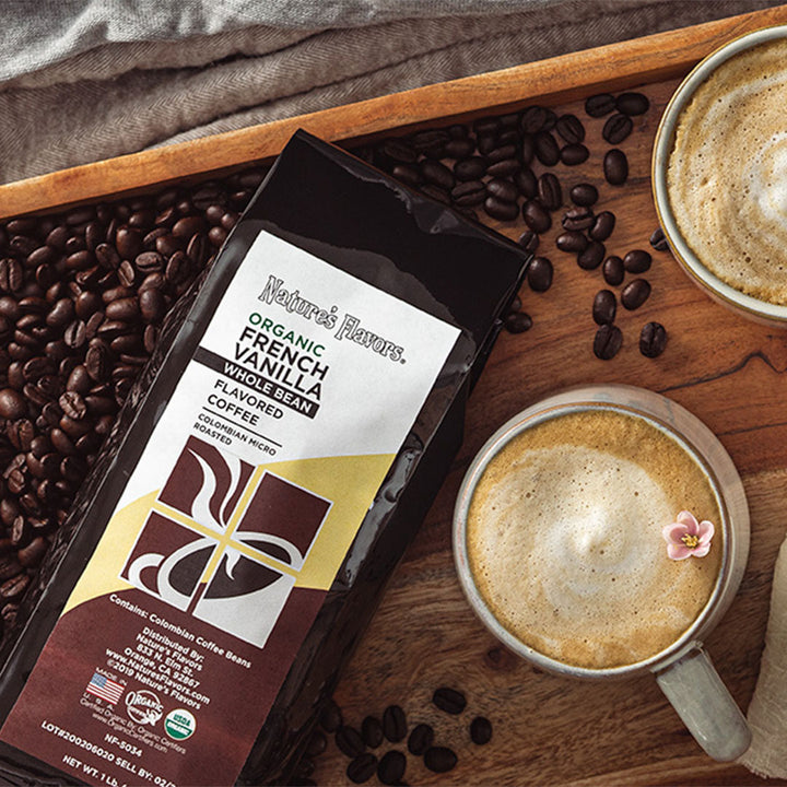 Bag labeled, "organic french vanilla whole bean flavored coffee" lying on a bed of coffee beans next to two cups of coffee. 