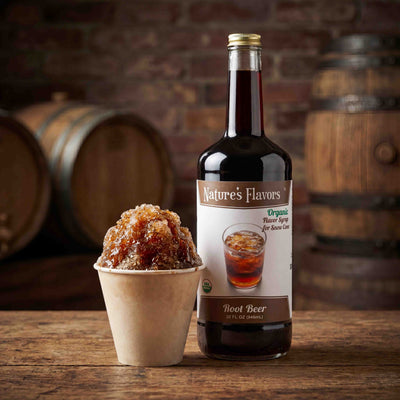 bottle labeled, "Organic Flavor Syrup For Snow Cone Root Beer" next to a cup of dark colored snow cone. 